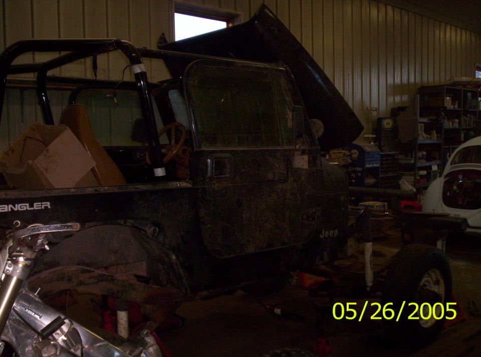 Black Jeep Wrangler with roll cage, hood open, and "Wrangler" text visible on the side