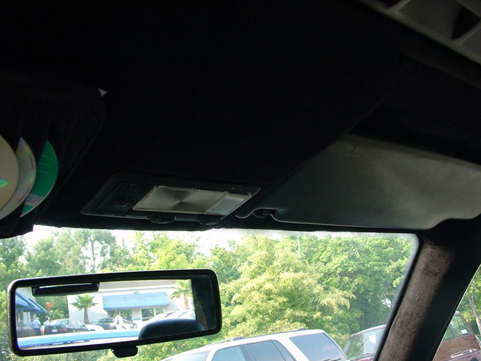 Interior view of car with CDs on visor and rearview mirror showing trees and buildings
