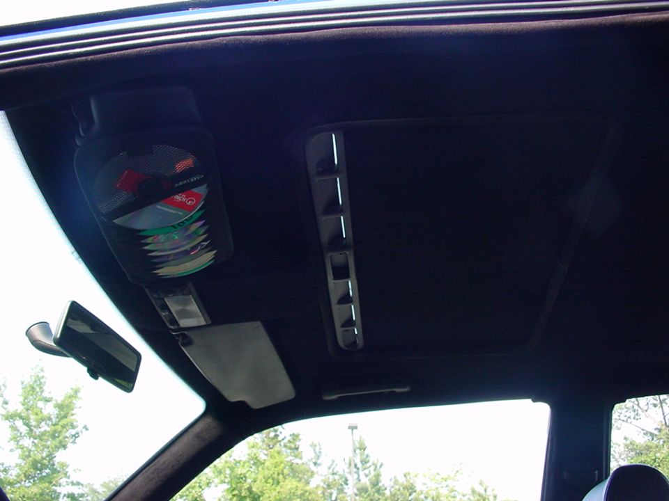 Car interior ceiling with a CD holder filled with discs, a sunroof, and a rearview mirror