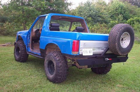 1987 Ford Bronco - This blue 1987 Ford Bronco is equipped with off-road tires and a custom rear bumper, with its doors removed.