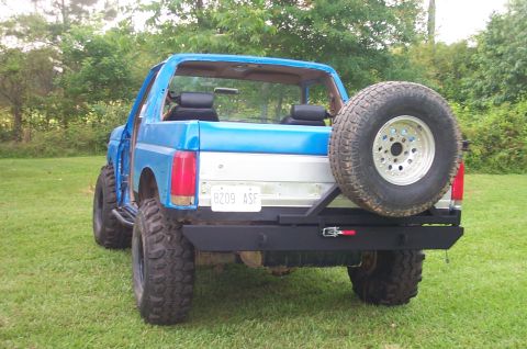 1987 Ford Bronco - Rear view of a blue Ford Bronco with a spare tire and custom bumper.