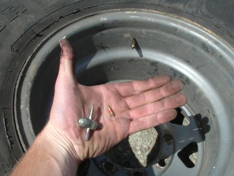 1989 Ford Bronco - A hand holds a tire valve stem tool and a valve core over a wheel rim, illustrating tire maintenance parts.