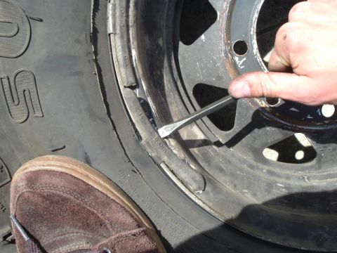 1989 Ford Bronco - Prying the tire bead off the wheel rim with a tool. A shoe is visible in the foreground.