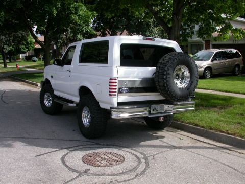Lifted white full-size Ford Bronco SUV with rear spare, three-quarter rear view