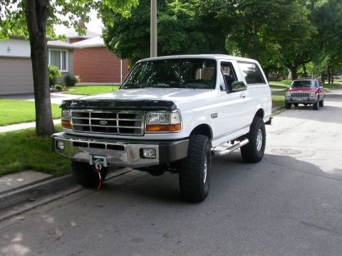 White Ford Bronco with aftermarket bumper and winch, parked on a residential street