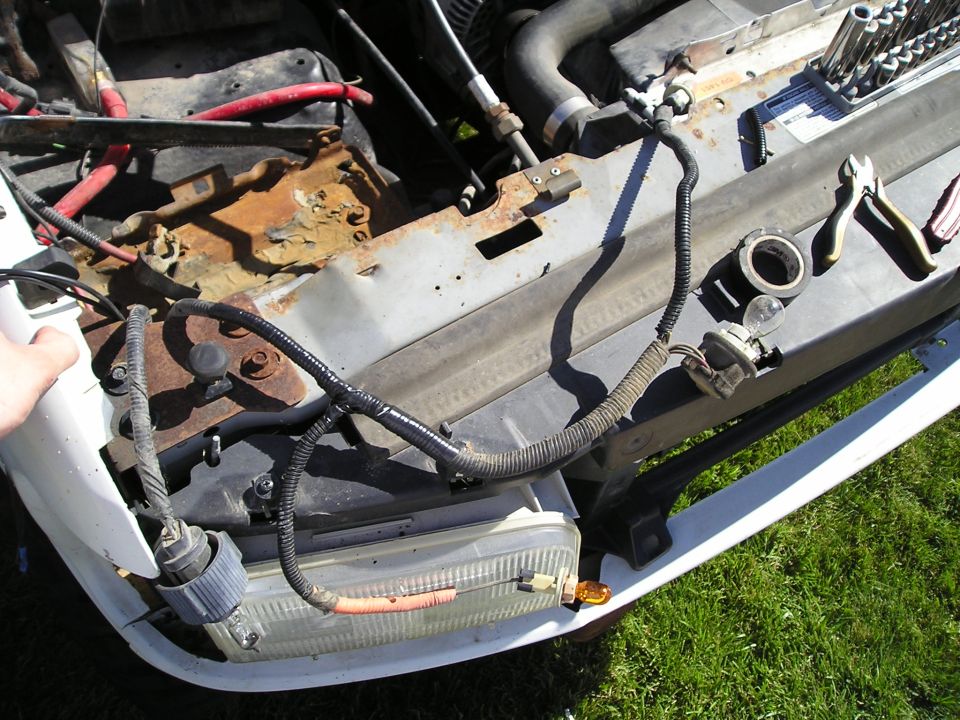 Open front end of a white truck showing bare core support, wiring harness and radiator removed