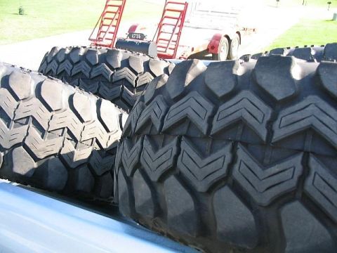 1986 Ford F-150 - A close-up view of several large, off-road tires loaded onto a vehicle, with a trailer visible behind them.