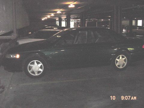 1995 Ford Taurus - A dark green 1995 Ford Taurus sedan is parked in a garage, viewed from the side with other vehicles nearby.
