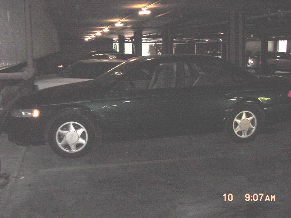 Dark green sedan shown in side view in a dark parking garage with headlights on
