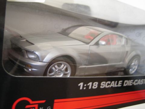 1990 Ford Bronco - silver-gray Ford Mustang coupe 1:18 scale die-cast model shown inside a black GT-branded display box.