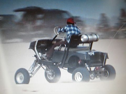 1990 Ford Bronco - Rear three-quarter view of a plaid-shirted rider on a tube-frame sand buggy with a cylindrical rear tank.