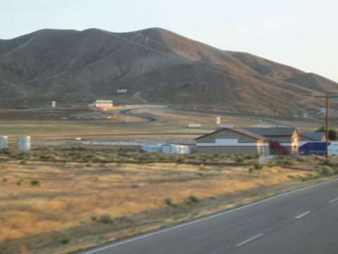 1990 Ford Bronco - road circuit and trackside buildings sit at the base of barren brown hills, viewed from across a highway.