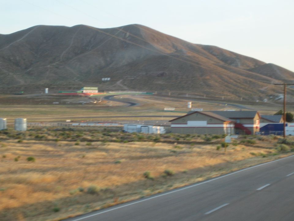 Racetrack and buildings at base of barren brown hills beside road
