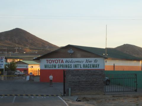 1990 Ford Bronco - low building with painted lettering reading Toyota Welcomes You to Willow Springs International Raceway at dusk.