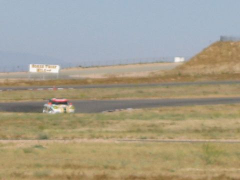 1990 Ford Bronco - distant, slightly blurred race car travels along a road course below a grassy embankment and Horse Thief Mile sign.