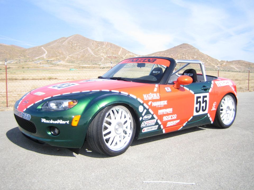 Green and orange Mazda Miata race car number 55 with white wheels