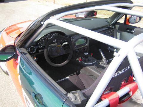 1990 Ford Bronco - stripped interior of a Miata race car showing a welded roll cage, digital dash, suede wheel and Sparco harness.
