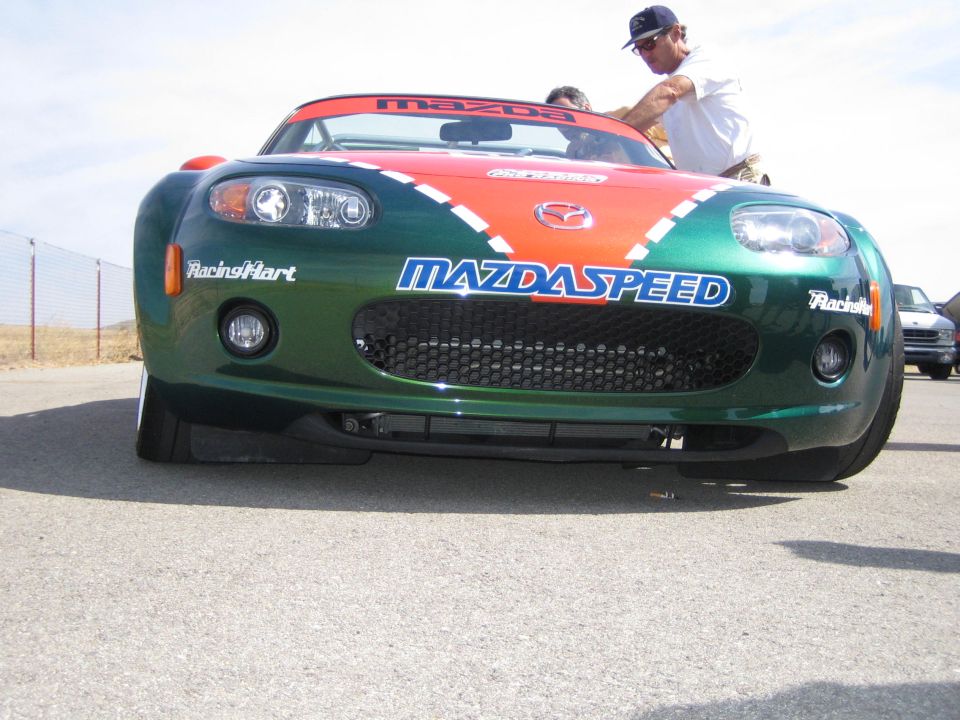 Green Mazda MX-5 roadster with Mazdaspeed and Racing Hart front-end decals at a track