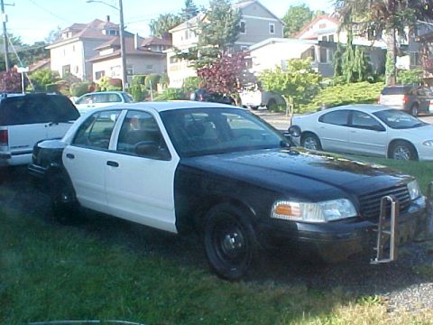 1999 Ford Crown Victoria - This two-tone sedan has a black front end and white rear. A white car is parked behind it.