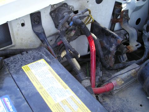 1990 Ford Bronco - Close-up view of engine bay components, including battery and wiring, with visible signs of rust.