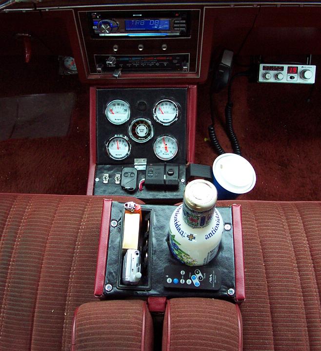 Car interior showing a CB radio, aftermarket gauges, and a bottle of antioxidant drink on the center console