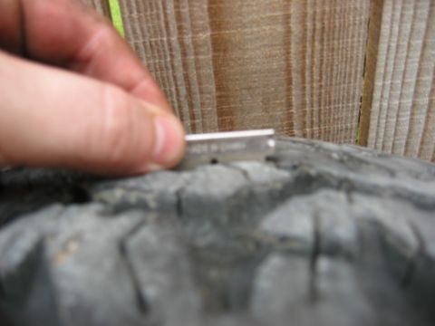 1986 Ford Bronco - A razor blade is used to inspect the tread depth of a tire, with a wooden fence in the background.