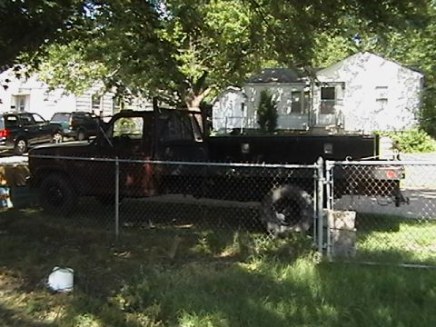 1986 Ford Bronco - Side view of a black pickup truck with a flatbed, parked behind a chain-link fence.