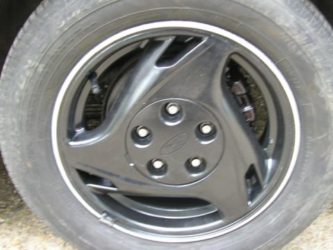 1990 Ford Probe - A close-up view of a car's wheel and tire, a black rim with a Ford emblem on the center cap.