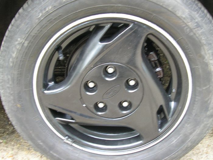 Close-up of a black car wheel with a Ford logo on the hubcap. Tire has a white stripe