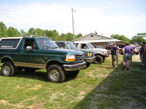 1996 Ford Bronco - A line of SUVs and trucks are parked on a grassy field near a building.