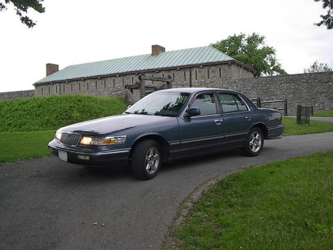 1985 Mercury Grand Marquis - Sedan parked on a road with a historic stone building in the background.