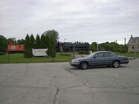 1985 Mercury Grand Marquis - A dark blue Mercury Grand Marquis is parked near a train museum on an overcast day.