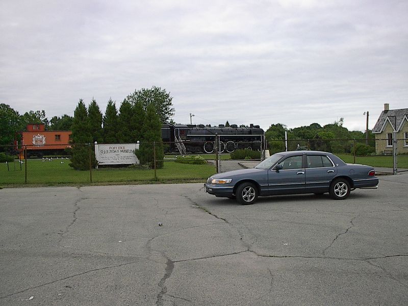 Blue-grey Mercury Grand Marquis parked beside the Fort Erie Railroad Museum steam engine