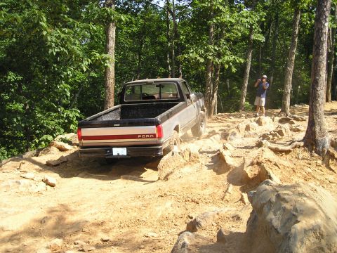 1996 Ford Bronco - Ford pickup truck driving on a challenging, rocky trail in a wooded area.