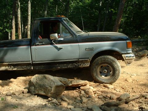 1985 Ford Bronco - This two-tone gray and black Ford F-250 pickup truck navigates a rocky trail, suggesting it is built for off-road use.