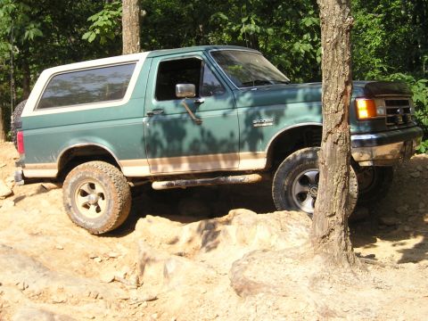 1996 Ford Bronco - Green Ford Bronco navigates a rocky trail, its tires gripping the uneven surface.