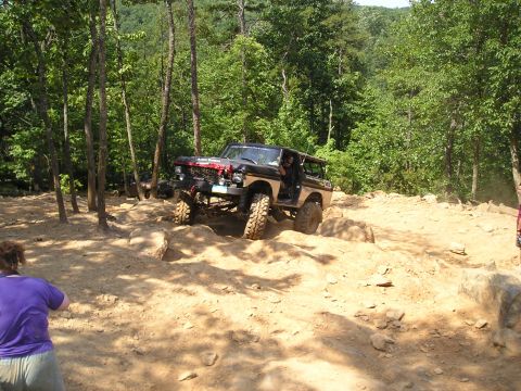 1996 Ford Bronco - Off-road SUV navigates a challenging rocky trail in a wooded area.