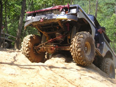 1996 Ford Bronco - A heavily modified off-road vehicle navigates a challenging dirt trail, its suspension and large tires.