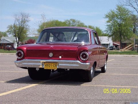 1960 Ford Falcon - The rear of a red 1960 Ford Falcon sedan is shown in a parking lot on a sunny day.