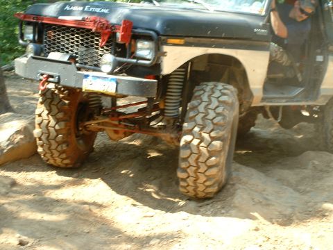 1985 Ford Bronco - Low front three-quarter view of a lifted black-and-tan Ford 4x4 with a doorless cab, showing the exposed solid front axle with red-painted…