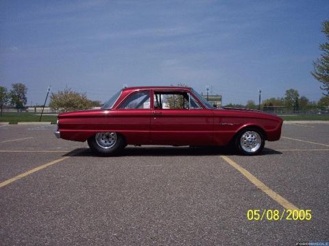 1960 Ford Falcon - A red 1960 Ford Falcon is parked in a lot on a sunny day, showing its side profile and custom wheels.