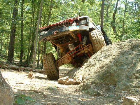1985 Ford Bronco - Off-road vehicle navigating a challenging rocky terrain in a forest setting.
