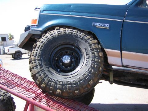 1994 Ford Bronco - Close-up of a 1994 Ford Bronco's front wheel and fender, showing off-road tires. Another vehicle is visible in the background.