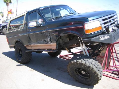 1994 Ford Bronco - This 1994 Ford Bronco is on jack stands, showing off its suspension and large tires. The driver's side door has visible damage.