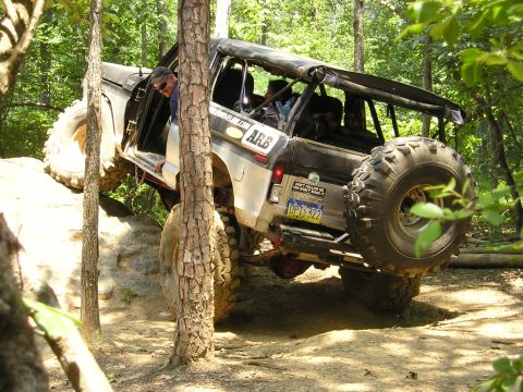 1996 Ford Bronco - Modified Ford Bronco tackling a rocky trail with its large tires and open doors.