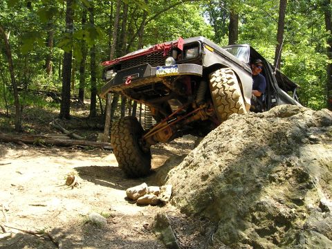 1996 Ford Bronco - An off-road SUV navigates a rocky trail in a wooded area, demonstrating its climbing capability.