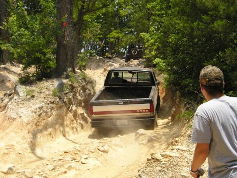 1996 Ford Bronco - A black Ford pickup truck navigates a dusty off-road trail, with another vehicle following behind.