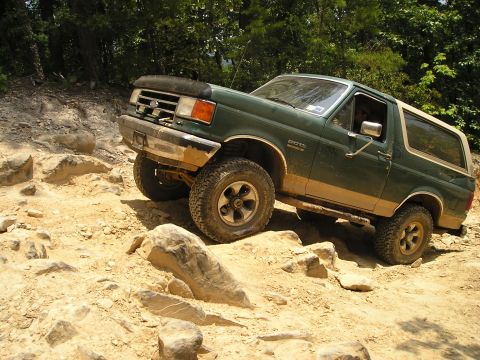 1996 Ford Bronco - A green Ford Bronco navigates a rocky off-road course, kicking up dust.