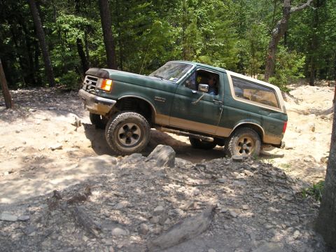 1996 Ford Bronco - This green Ford Bronco is shown tackling a challenging rocky trail, demonstrating its off-road capabilities.