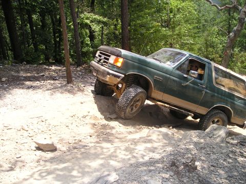 1996 Ford Bronco - 1996 Ford Bronco tackling a challenging off-road course in a wooded area.